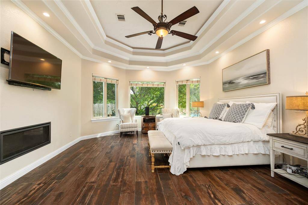 The primary suite is a serene retreat, designed with elegance in every detail. A cozy fireplace and inviting sitting area framed by bay windows create the perfect space to relax. Tray ceilings, recessed lighting, and an elegant ceiling fan add layers of sophistication and comfort.