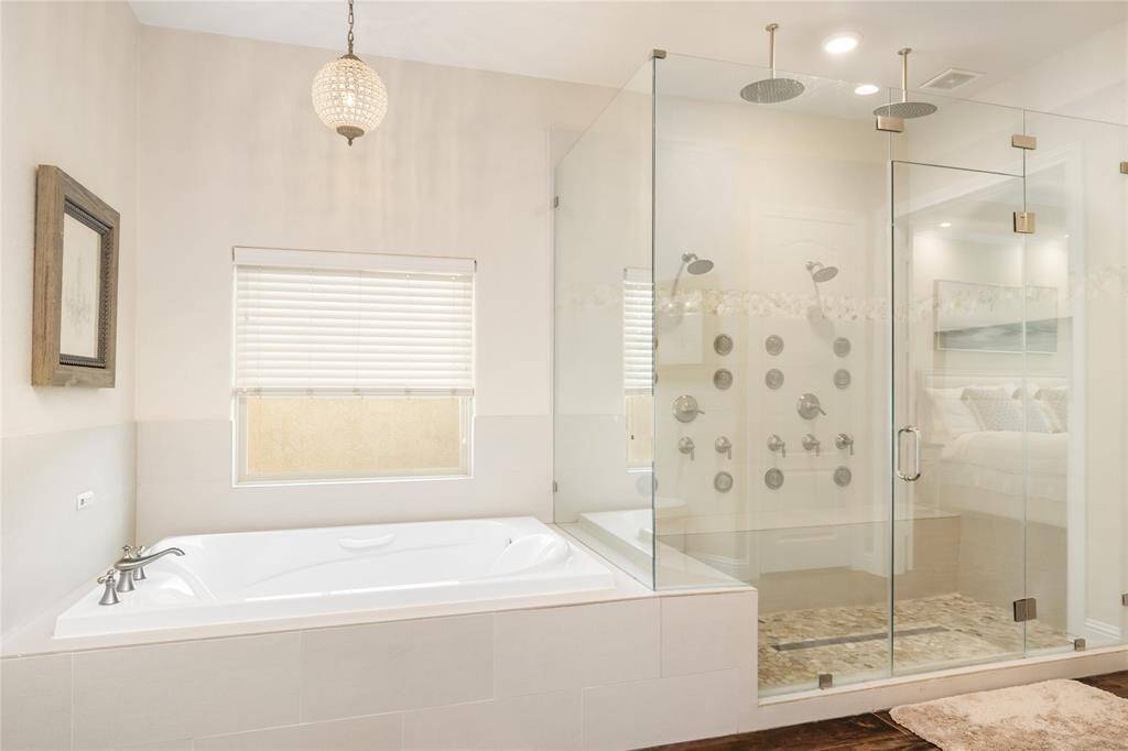 Beneath an elegant light fixture, the soaking tub offers a tranquil escape. Nearby, the oversized shower is equipped with multiple shower heads—including rain and standard options—allowing you to tailor every detail to your perfect setting. With an array of thoughtfully designed controls, luxury meets personalization in this spa-like retreat.