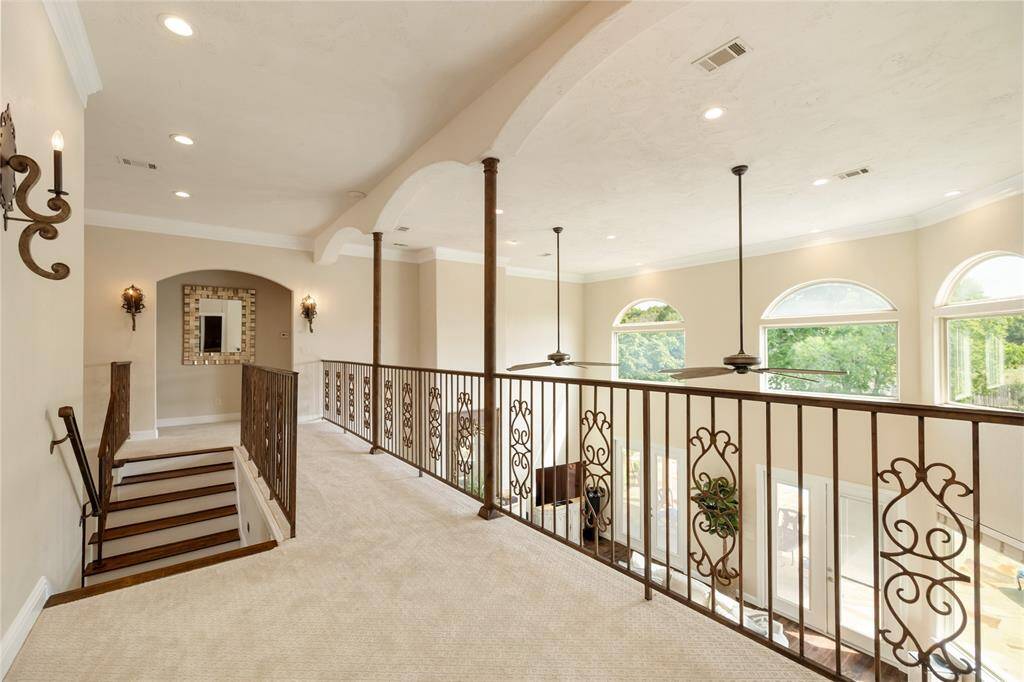 Peer over the grand living room from the second-story balcony, where iron railings, graceful arched openings, and candle-style sconces blend beautifully to create a scene of refined elegance. This vantage point showcases the home’s sophisticated architectural details.