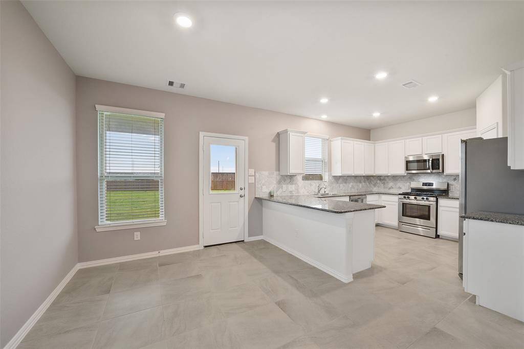 Modern kitchen with light gray tile flooring, white cabinetry, and stainless steel appliances. The bright and cheery breakfast area benefits from lots of natural light.