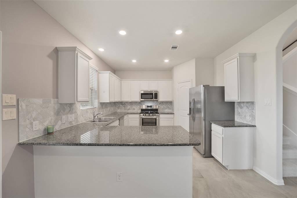 The modern kitchen has granite countertops, white cabinetry, and stainless steel appliances.