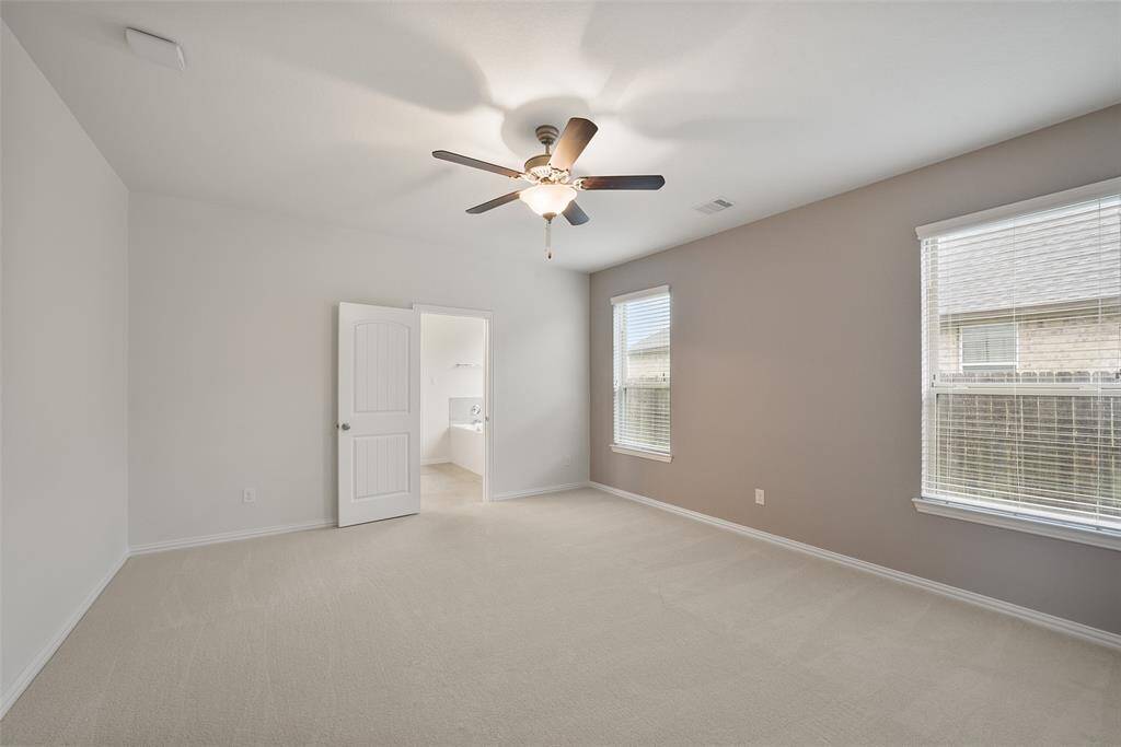 This spacious master suite features neutral carpeting, a ceiling fan, and two large windows for natural light.