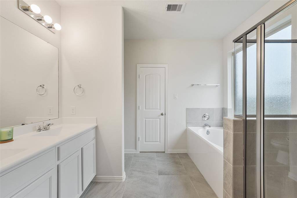 The master bath features a modern design with a spacious double vanity, a large mirror, and stylish lighting. It includes a separate bathtub and a glass-enclosed shower, offering both functionality and elegance.