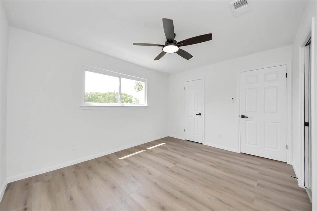 This bright and airy secondary bedroom features fresh paint, wide-plank flooring, and a modern ceiling fan. A large horizontal window fills the space with natural light, creating a comfortable and inviting atmosphere.