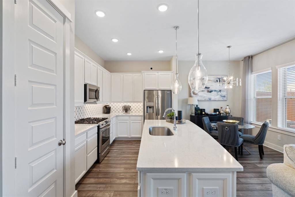 The kitchen features quartz countertops, a large island with a built-in sink, stainless steel appliances, a pantry, and a dining area.