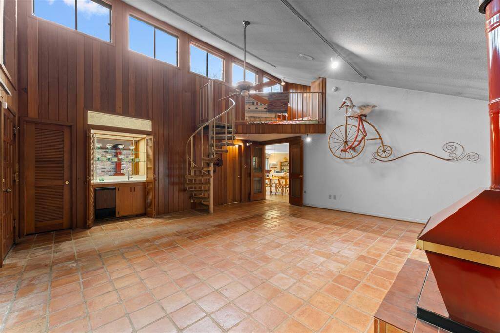 Whimsical vaulted den with Saltillo tile flooring, walk in closet, wet bar, with laundry and half bath just out of view through doorway to right of spiral staircase.