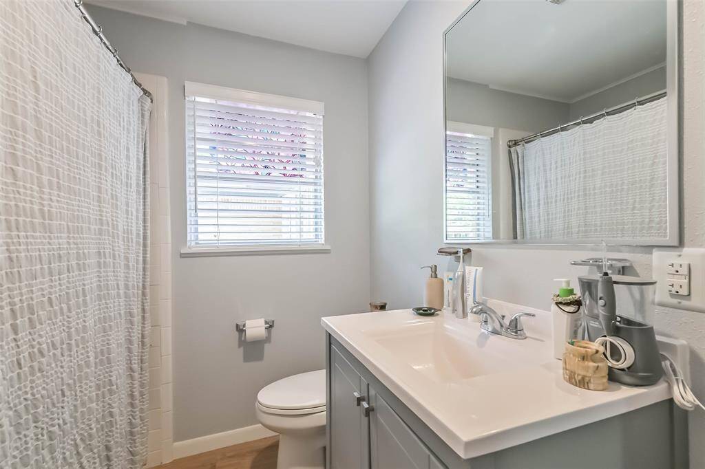 Hall bathroom includes designer vanity, framed mounted mirror, window overlooking side patio and tub with crisp, white tile surround