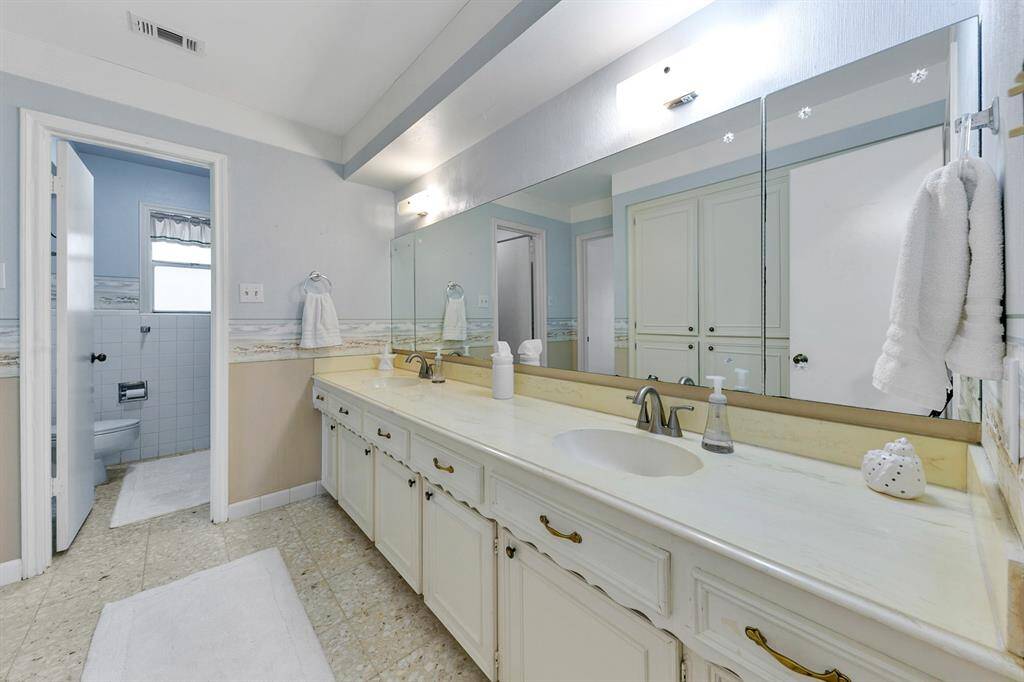 This bathroom features a long vanity with ample storage and a large mirror. It has a neutral color scheme, overhead lighting.