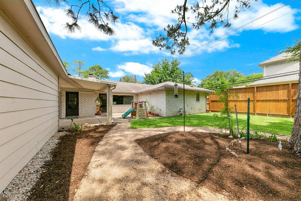 This backyard features a cozy, landscaped area with a mix of mulch and grass, bordered by a wooden privacy fence. It includes a small playset, bird feeder, and covered patio, offering a perfect space for outdoor relaxation and family activities.
