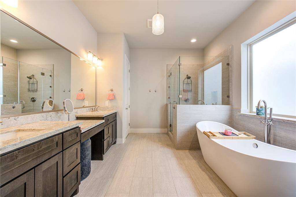 Spa-like primary bath with double sinks, makeup vanity, freestanding soaking tub, frameless glass shower, and a private water closet.