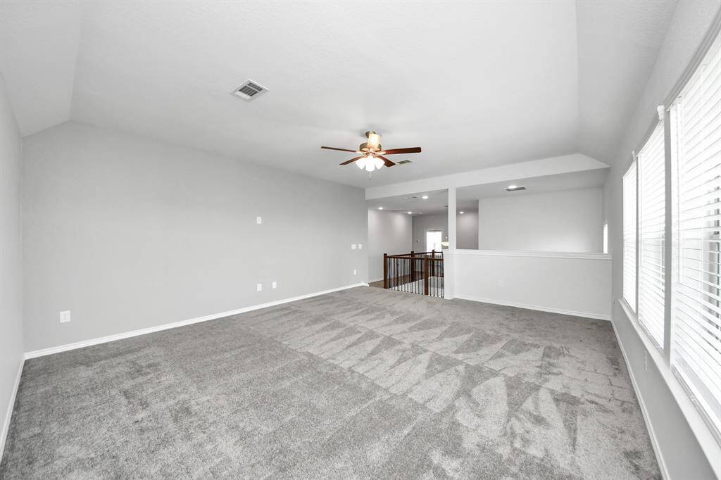 Large upstairs game rm living area with plush carpet, ceiling fan, and open railing overlooking the first floor.