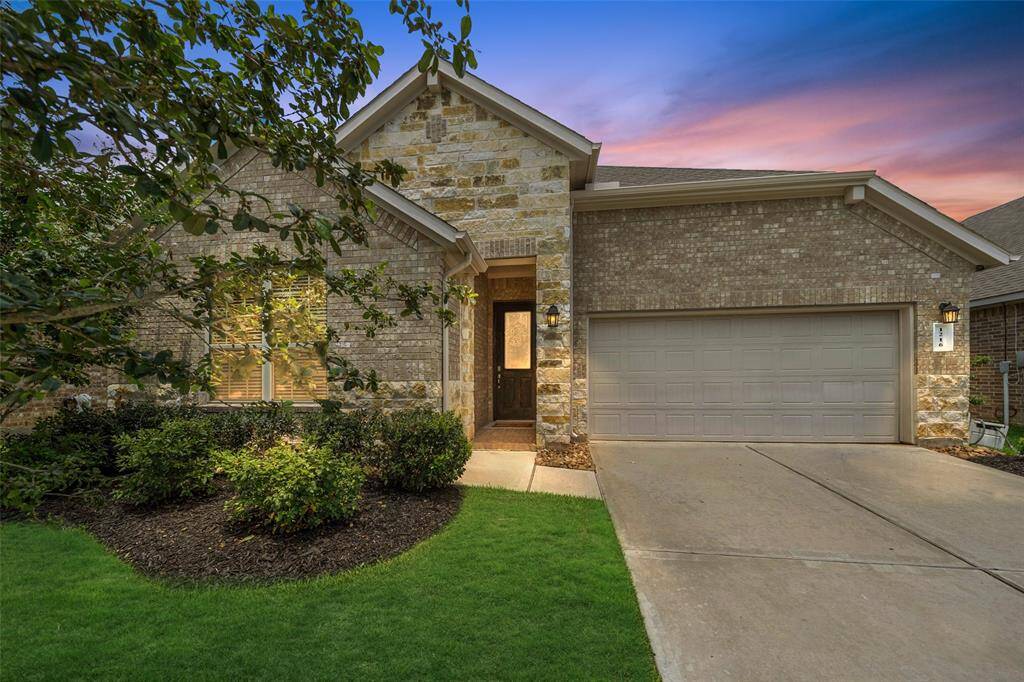 This home features a brick and stone exterior with a welcoming entrance. It includes a well-maintained lawn, landscaped shrubs, and a spacious 3-car garage.