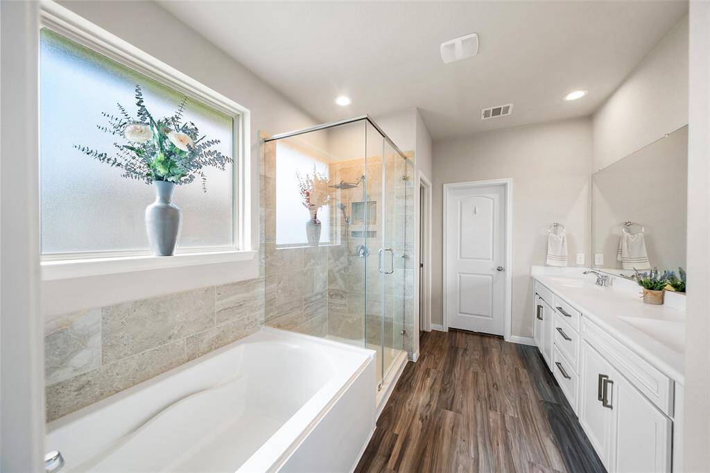 This bathroom features a spacious layout with a large bathtub, a glass-enclosed shower, and a dual-sink vanity. It has elegant tile accents and ample natural light from a frosted window.