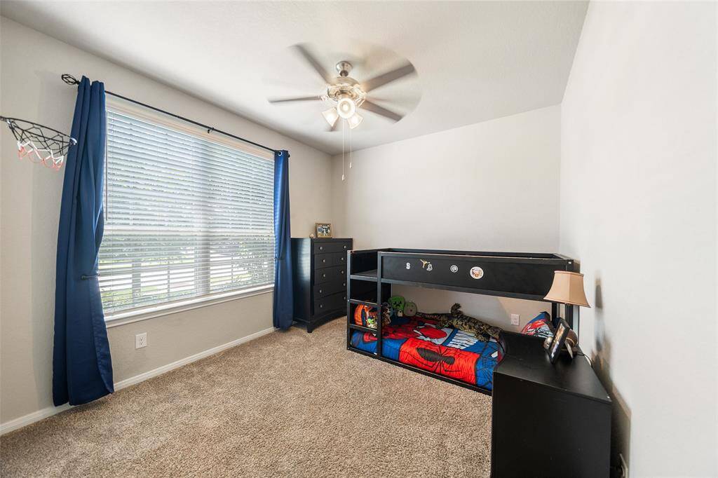 This secondary bedroom features a cozy setup with carpet flooring, a ceiling fan, and a large window.