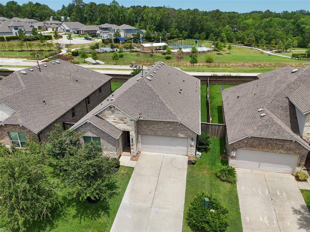 This aerial view showcases a well-maintained front yard and a 3-car garage. The neighborhood features neatly arranged houses, lush greenery, and a nearby recreational area with a pool, providing a pleasant and family-friendly environment.