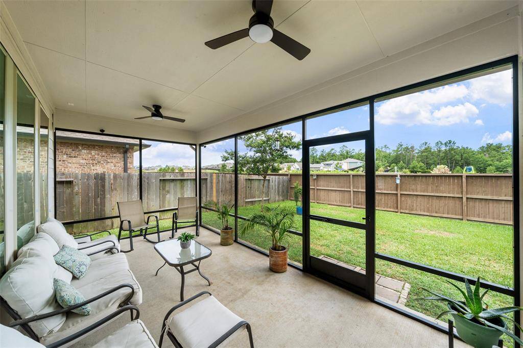 The back patio showcases a practical screened-in patio with ceiling fans overlooking a fenced backyard with a lush lawn. Ideal for relaxation and outdoor enjoyment.