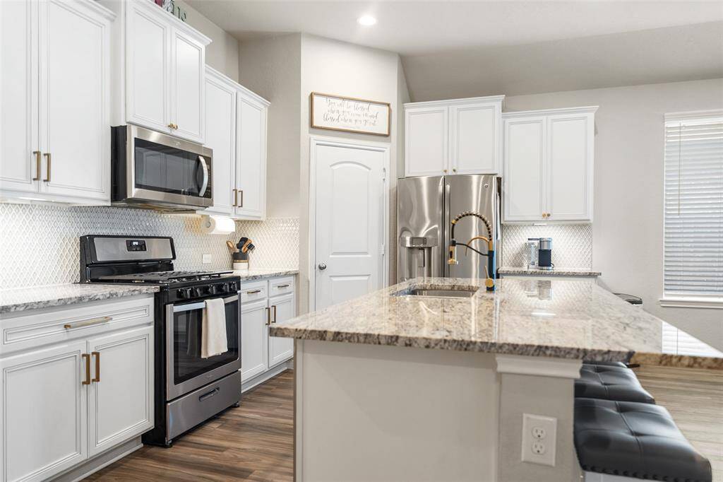 This kitchen features a large granite island with seating. It has a sleek backsplash and ample natural light, creating a bright and inviting space.