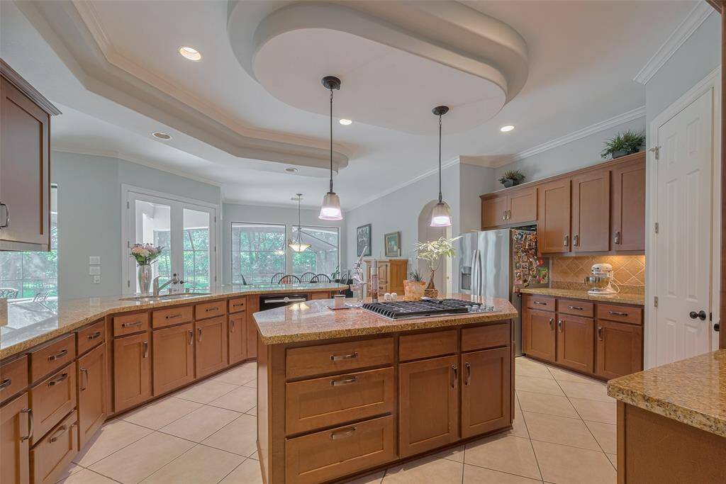 This stunning island kitchen boasts numerous updates, beginning with shaker-style cabinets beautifully stained and complemented by modern hardware. The impressive high ceilings feature intricate detailing, enhanced by recessed lighting and stylish pendant lights above the island.