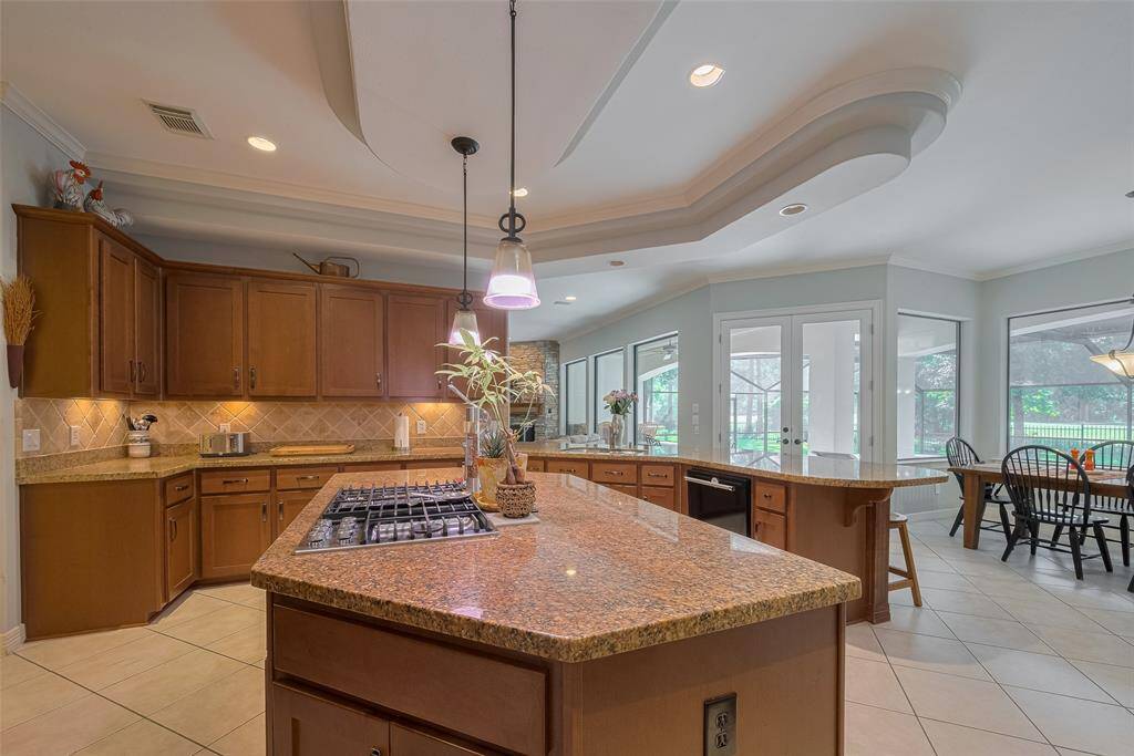 Most appliances were updated in 2023, including the 5-burner gas cooktop on the island. The kitchen features rich granite countertops, a travertine diagonal tile backsplash, and under-cabinet lighting—all framed by large windows with views of the pool and golf course.