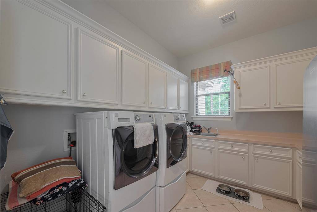 Located just off the oversized 3-car garage—featuring a 2-car bay on one side and a single bay with extra workspace and a mud sink on the other—is this spacious laundry room. It offers plenty of room for a second refrigerator, abundant cabinetry, a sink, ample counter space, and more!