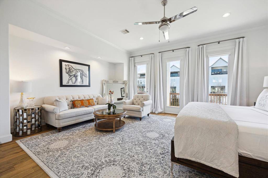 The spacious primary bedroom has a large balcony fronting the water, large windows and a cozy sitting area. The light color palette and modern ceiling fan create a serene, airy atmosphere.