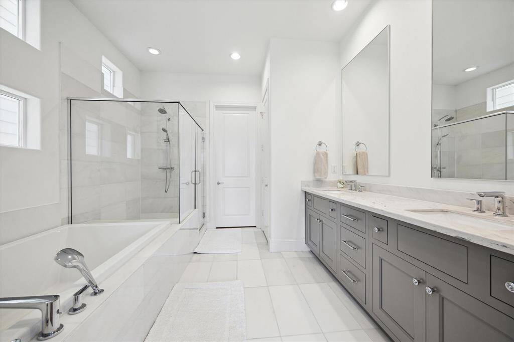 The primary bathroom features a sleek double vanity with ample storage, modern fixtures, and two large mirrors. The frameless shower and soaking tub add to the elegance.