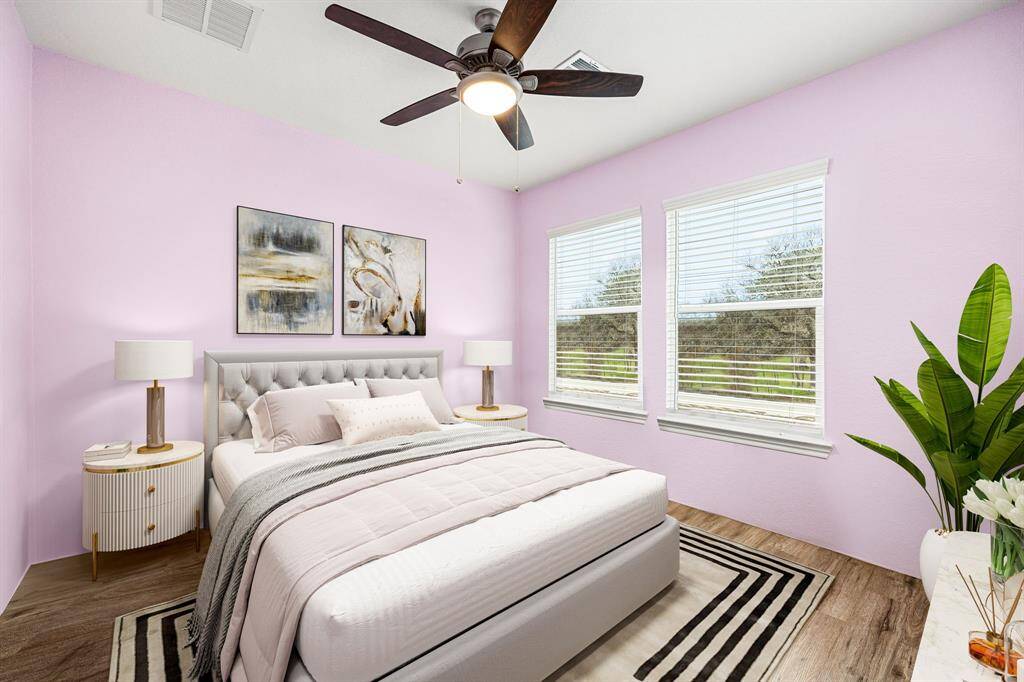 Secondary bedroom features warm vinyl plank, custom paint, dark stained ceiling fan with lighting and a large window with privacy blinds.