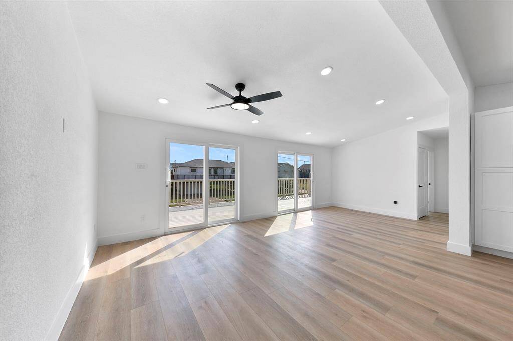 Bright and spacious living area with light wood flooring and a modern ceiling fan. The room features large sliding glass doors leading to a deck, allowing for plenty of natural light.