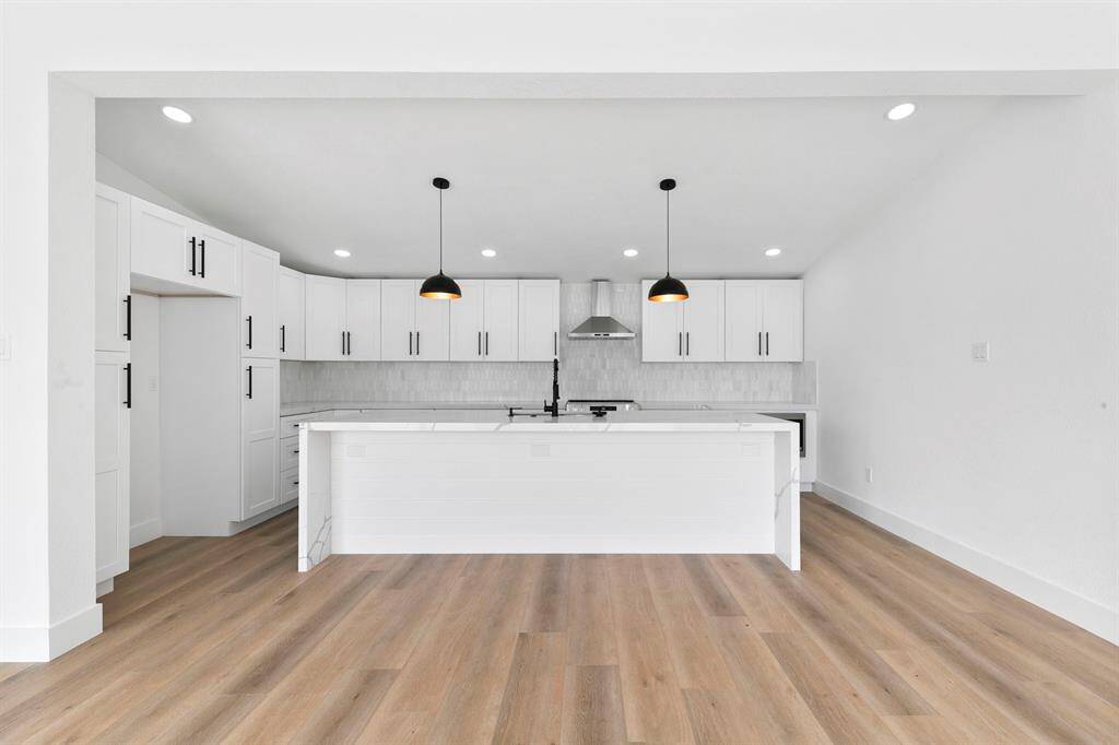This photo showcases a modern kitchen with a spacious open layout. It features sleek white cabinetry, a large island with pendant lighting, and stainless steel appliances, all complemented by light wood flooring.