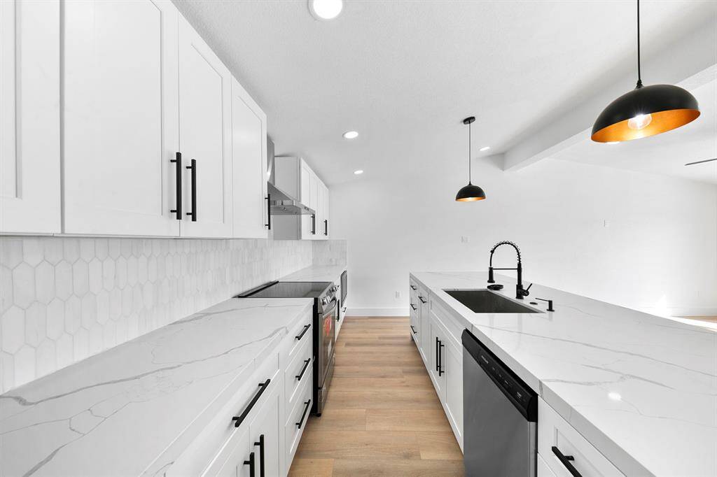 Modern kitchen with sleek white cabinetry, marble countertops, and black hardware. Features a stylish hexagonal tile backsplash, stainless steel appliances, and pendant lighting over the island with integrated sink. Bright and open layout with light wood flooring.