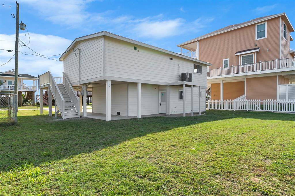 Elevated home with a spacious grassy yard, featuring an external staircase and a covered ground-level area. Ideal for flood-prone areas.
