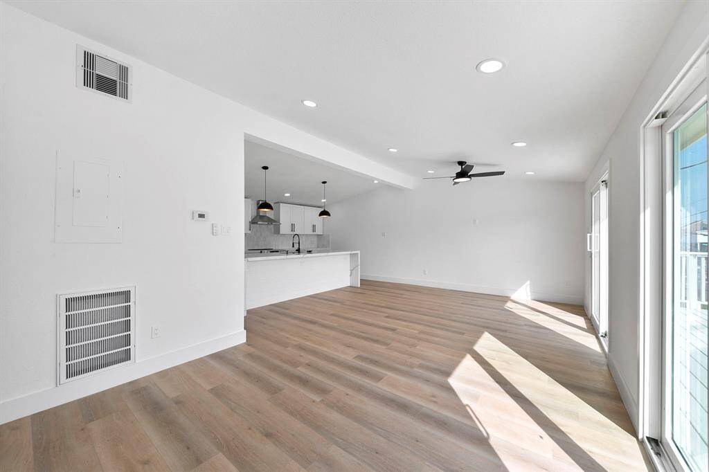 Bright and spacious open-concept living area with light wood flooring, modern kitchen with pendant lighting, and abundant natural light from large windows.