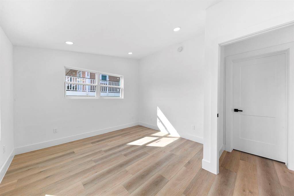 Bright, minimalist room with light wood flooring, white walls, and recessed lighting. It features a small window for natural light and a modern door, ideal for a cozy space.