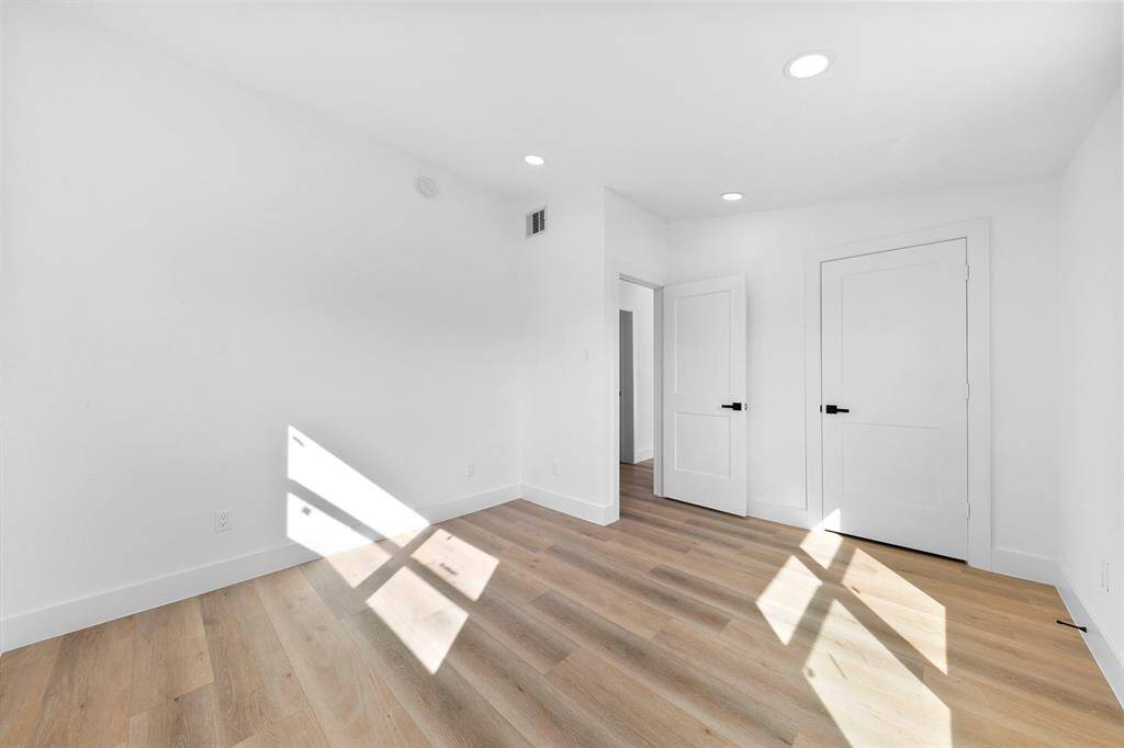 This photo shows a bright, airy room with white walls, light wood flooring, and recessed lighting. It features two white doors and ample natural light streaming through a window, creating a fresh and inviting atmosphere.