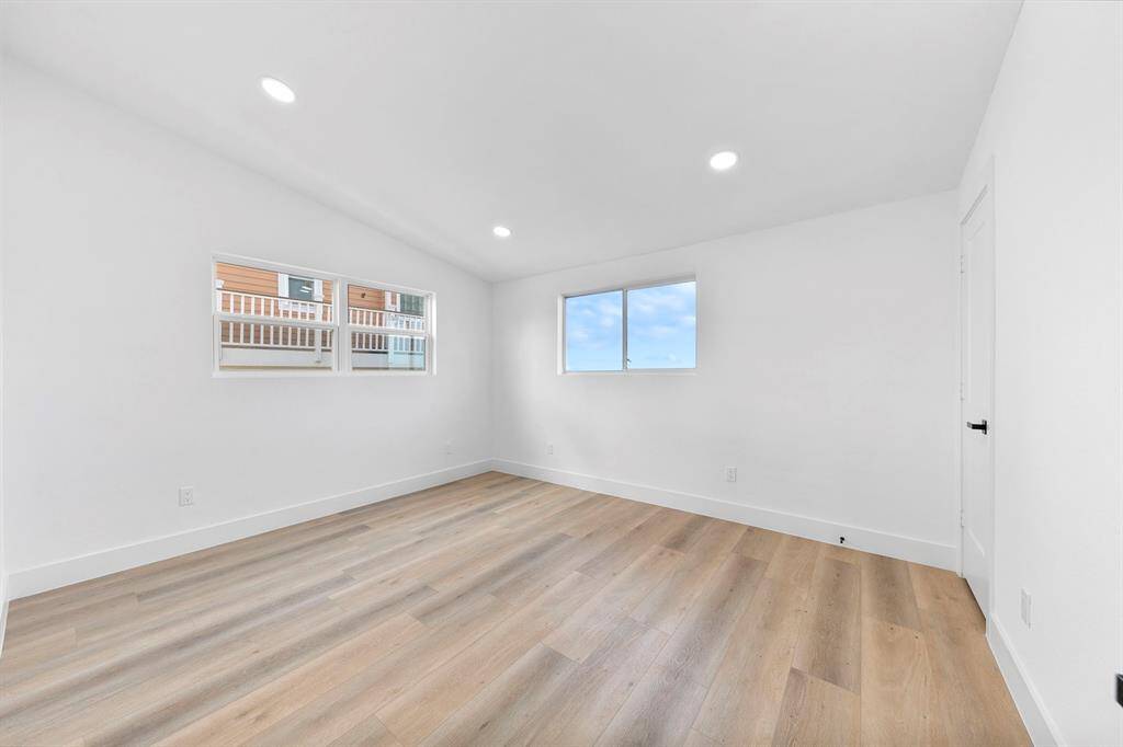This room features bright, white walls and wood flooring, offering a fresh and spacious feel. Two windows provide ample natural light, enhancing the open atmosphere.