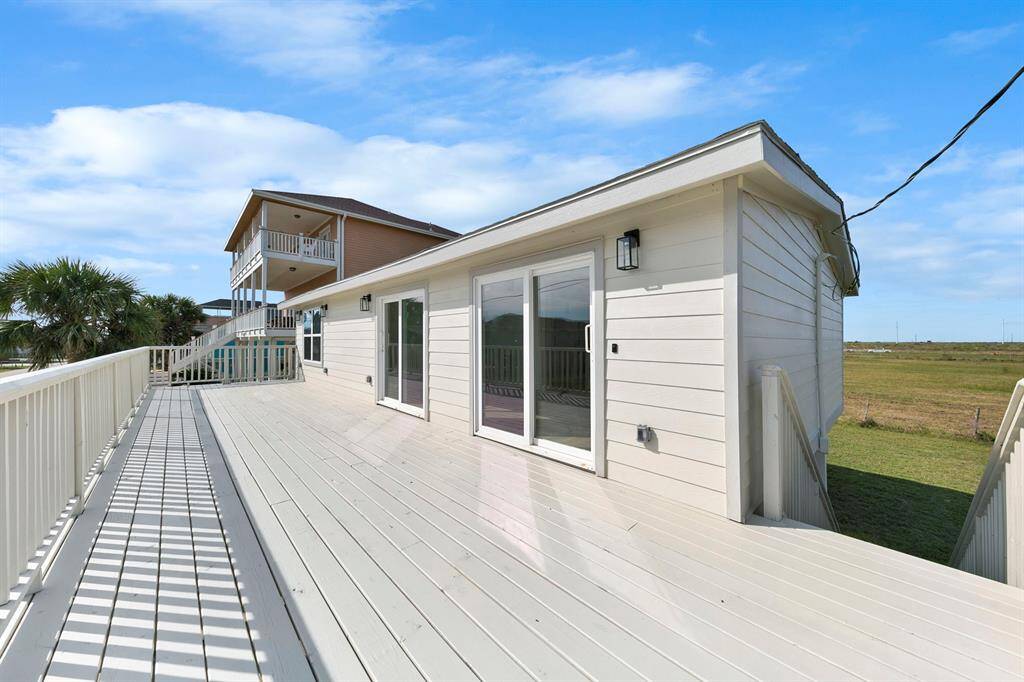 This photo showcases a modern home with a spacious, sunlit deck, perfect for outdoor relaxation. It features large sliding glass doors and a scenic view of open green space, providing a serene and inviting atmosphere.