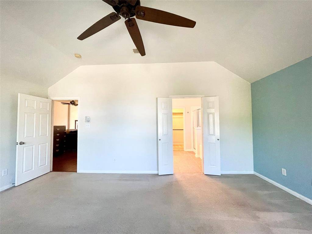Spacious main bedroom with vaulted ceiling, ceiling fan, and carpeted floor. It features a walk-in closet and en-suite bathroom, with double doors leading to both.