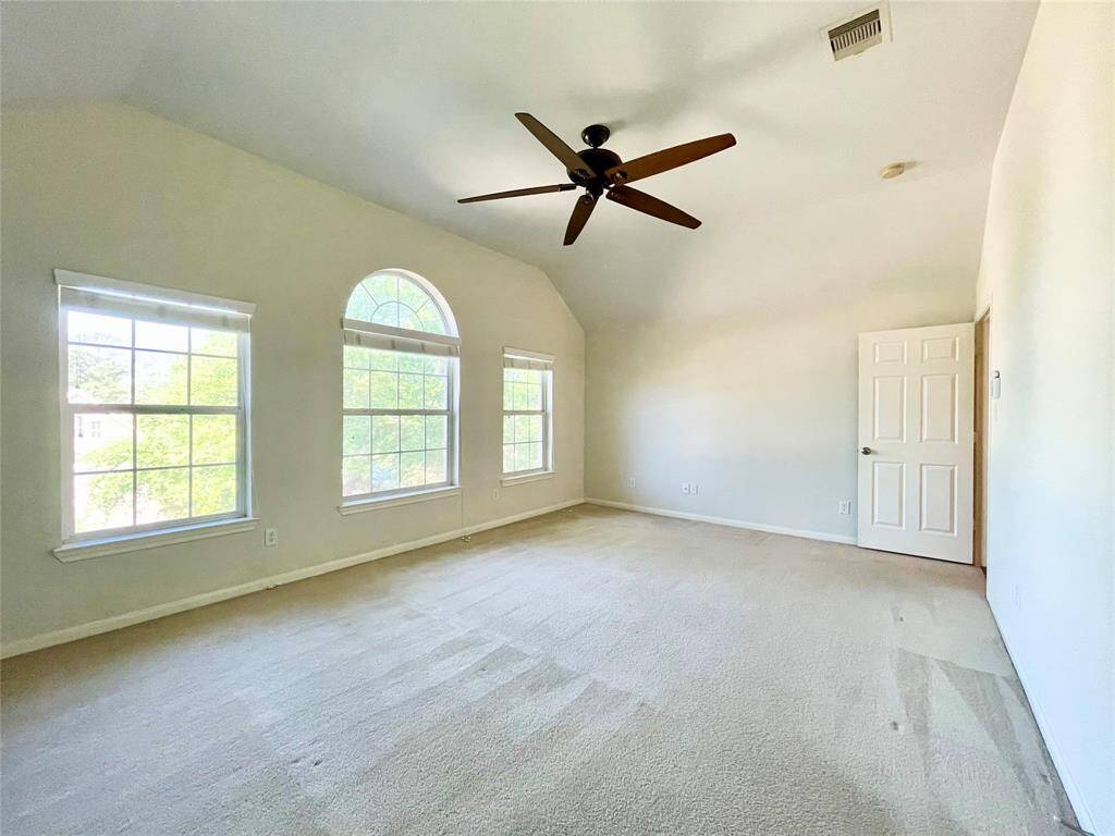 This spacious main bedroom features high ceilings, a large ceiling fan, and three large windows, including an arched window, providing abundant natural light.