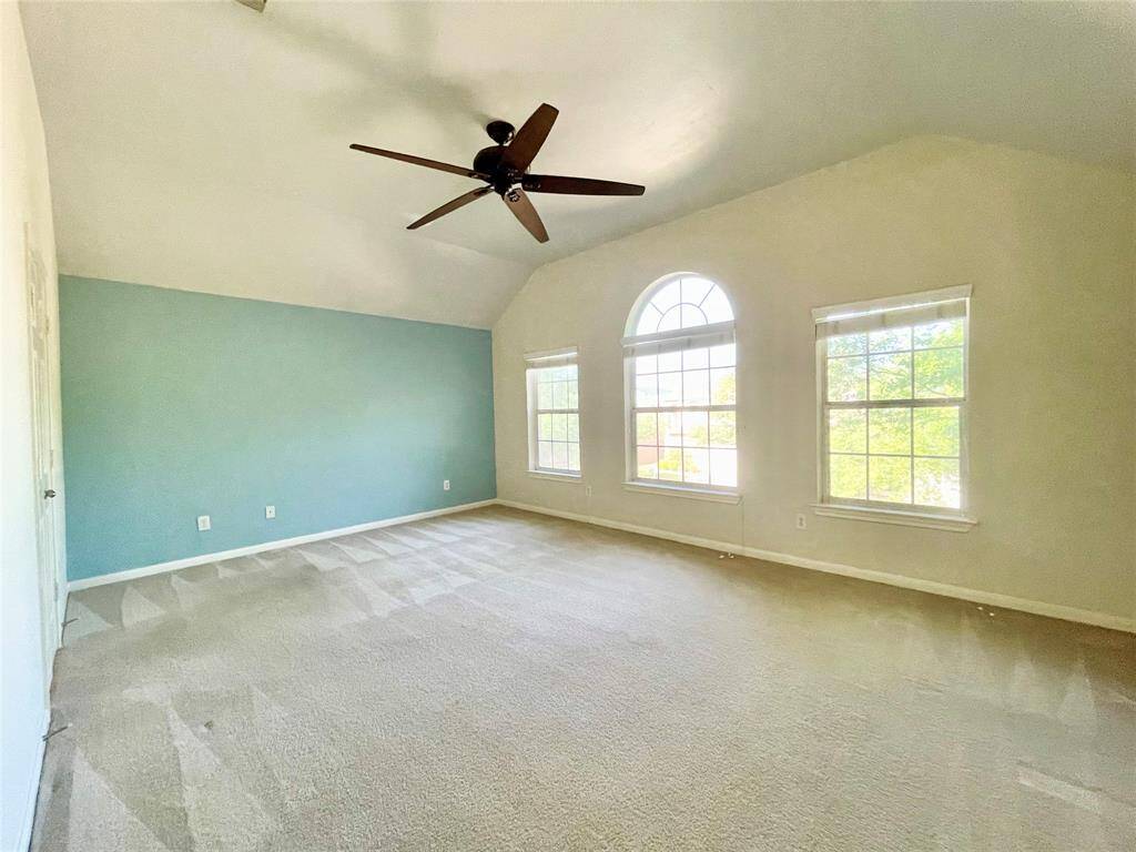 This spacious main room features a vaulted ceiling, large arched windows, a tasteful accent wall, and a ceiling fan, creating an inviting and airy atmosphere.