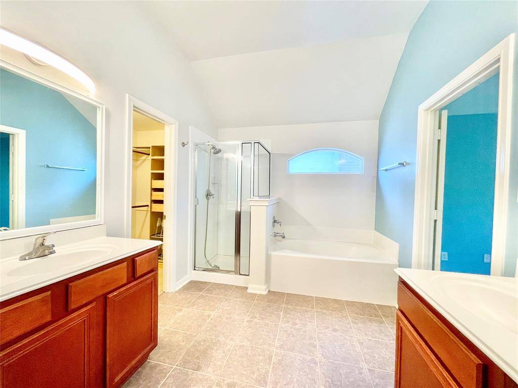 Master bathroom features a double vanity with wooden cabinets, a glass-enclosed shower, and a separate bathtub. The room is bright with light blue walls and includes a walk-in closet.