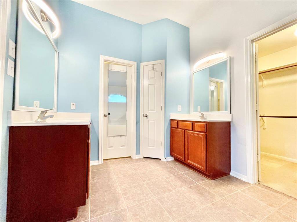 Master Bathroom features dual sinks with wood cabinets, a soothing blue wall color, and modern lighting. It includes a spacious walk-in closet and a separate shower area for convenience.