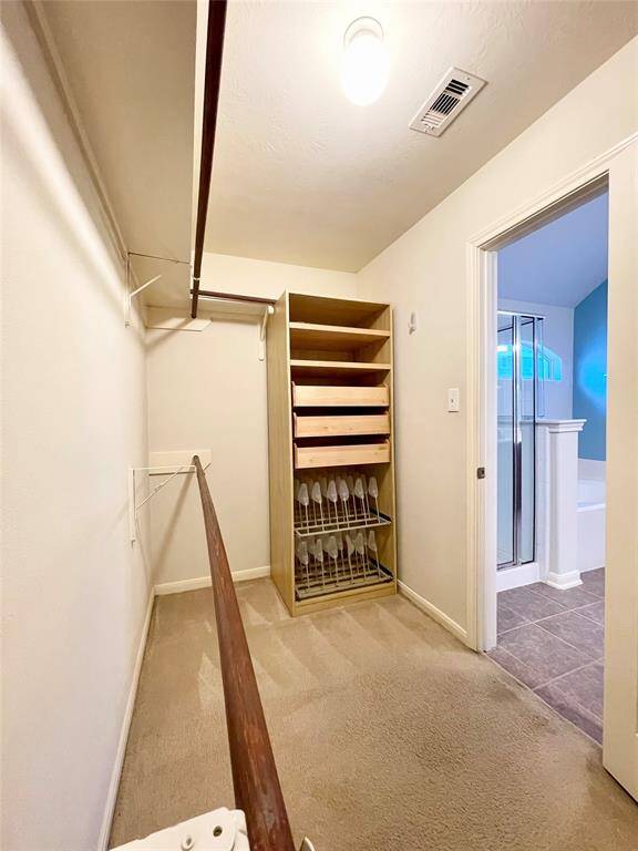 Spacious walk-in master closet with carpeted flooring, shelving, and ample hanging space.