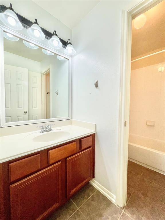 Bathroom # 2, Bathroom with a vanity featuring a large mirror and multiple lights. It has a wooden cabinet below the sink and a tiled floor. There's an adjacent door leading to a bathtub area.