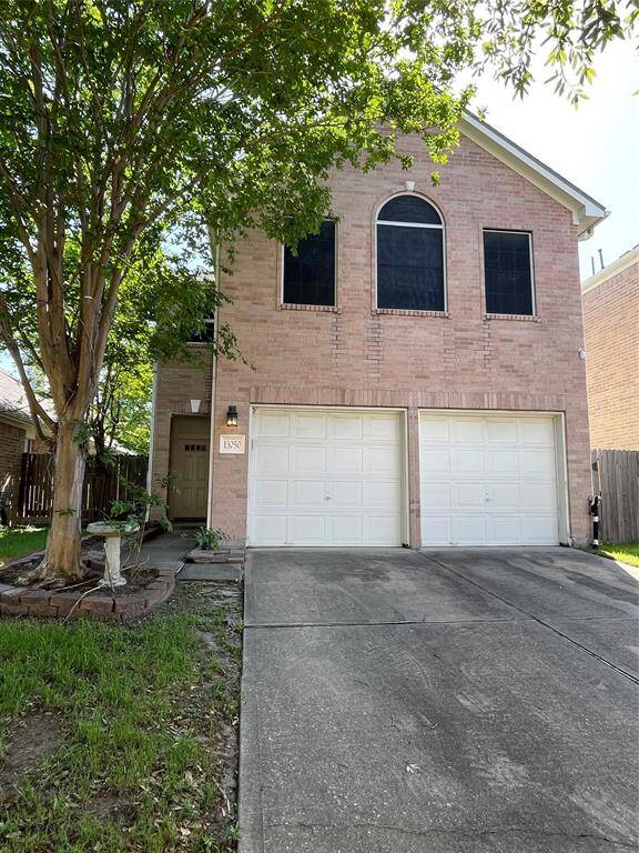 This two-story brick home features a double garage. It has a charming front yard with mature trees providing shade and a welcoming entrance.