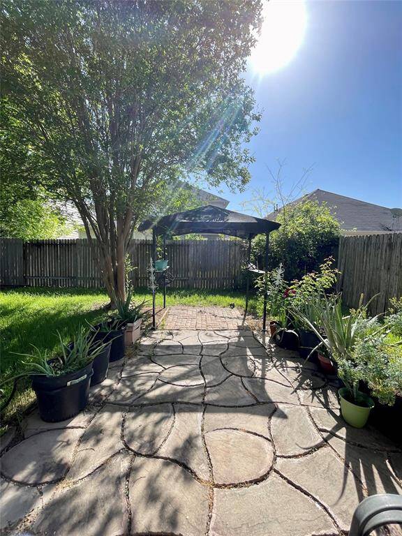 Charming front shaded by a nice tree, surrounded by potted plants and greenery.