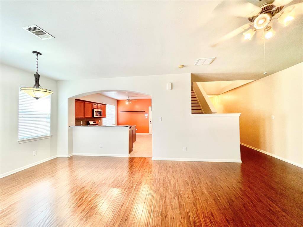 Spacious and bright open-concept living area with hardwood floors, a ceiling fan, and a view into the kitchen.