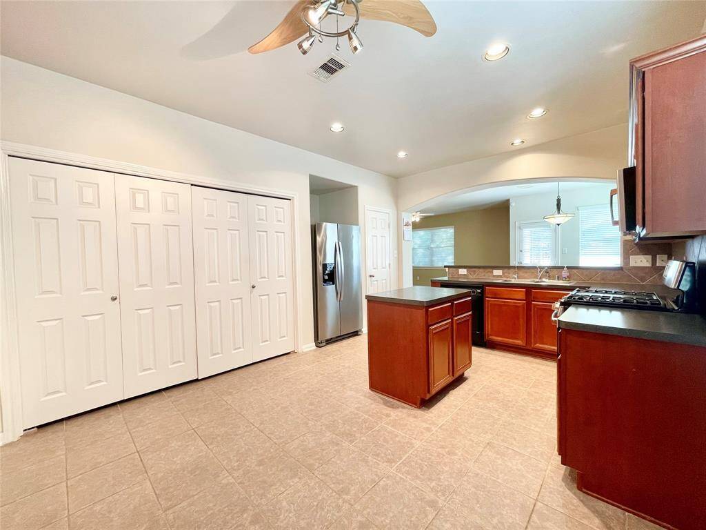 Spacious kitchen with modern stainless steel appliances, ample cabinetry, and a central island. Features recessed lighting, tile flooring, and a ceiling fan. Adjacent to a dining area with large windows for natural light.