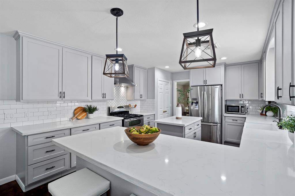 Sleek quartz countertops, soft gray cabinetry, and stainless steel appliances bring a modern feel to this thoughtfully designed culinary space.