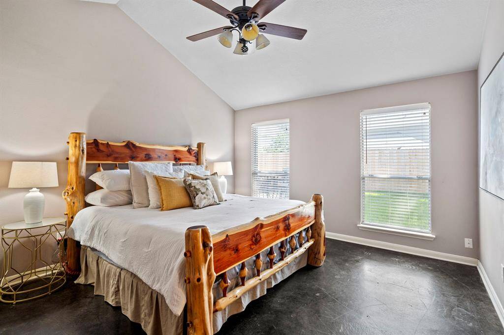The spacious primary bedroom features soaring ceilings, neutral tones, and abundant natural light from dual windows overlooking the backyard.