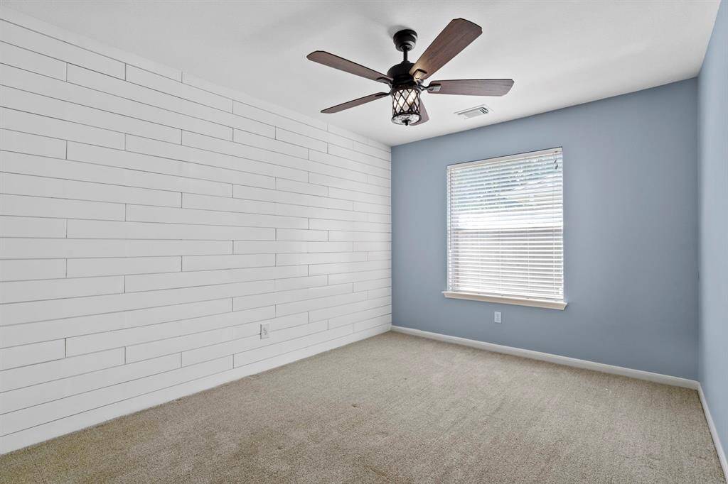 This bright and cheerful bedroom features a custom white shiplap accent wall, soft carpet, and a modern ceiling fan.